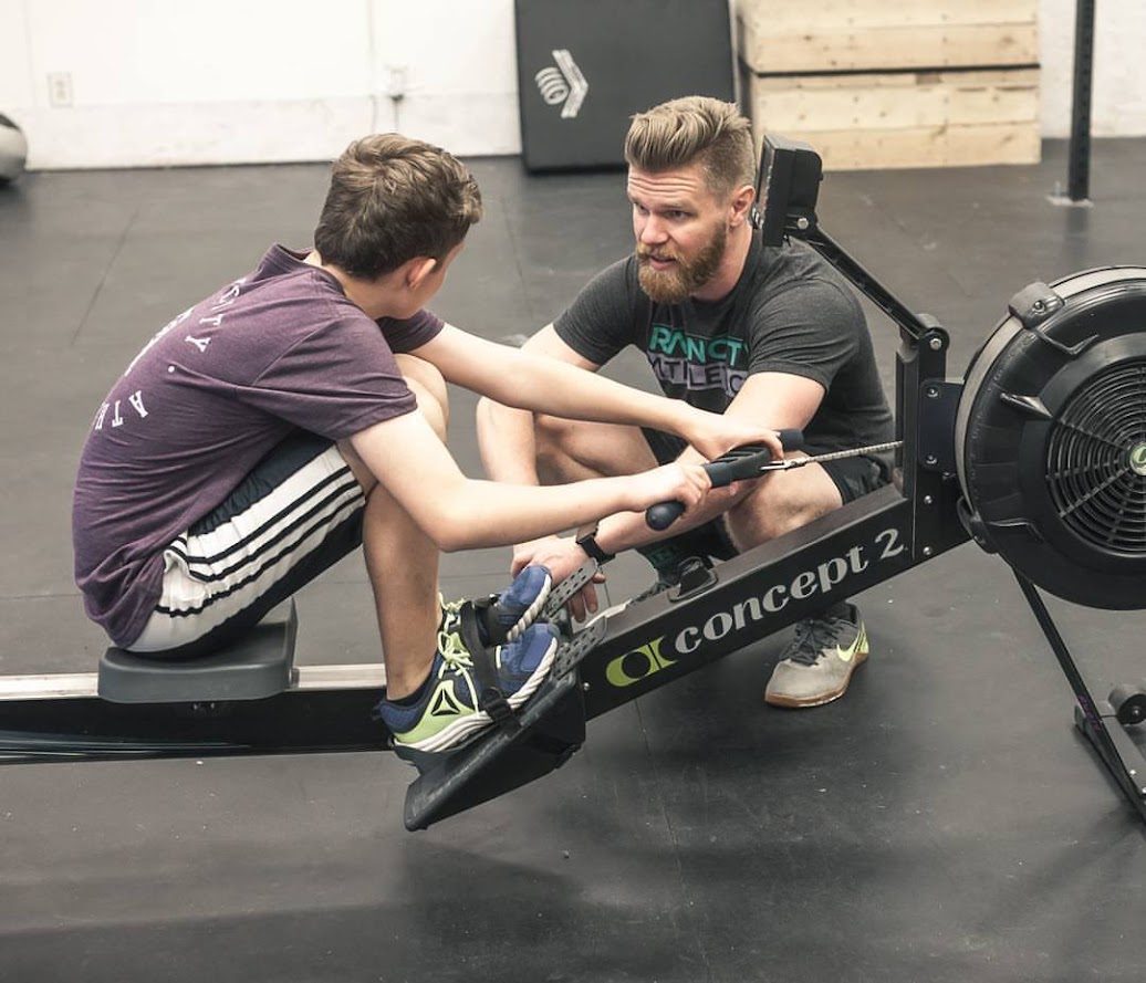 Coach Thor coaching a young athlete on a rowing machine