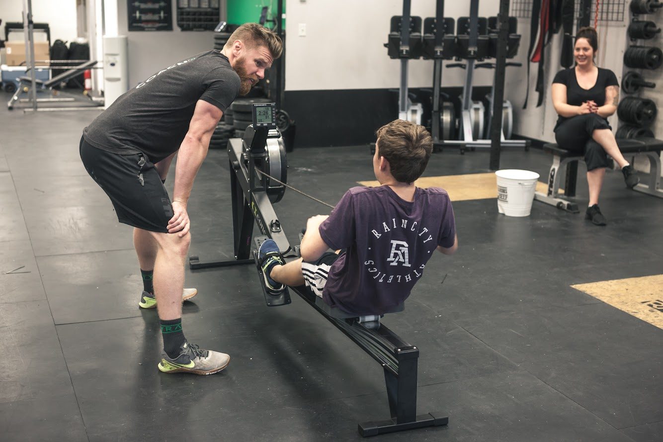 A student on a rowing machine while Coach Thor watches